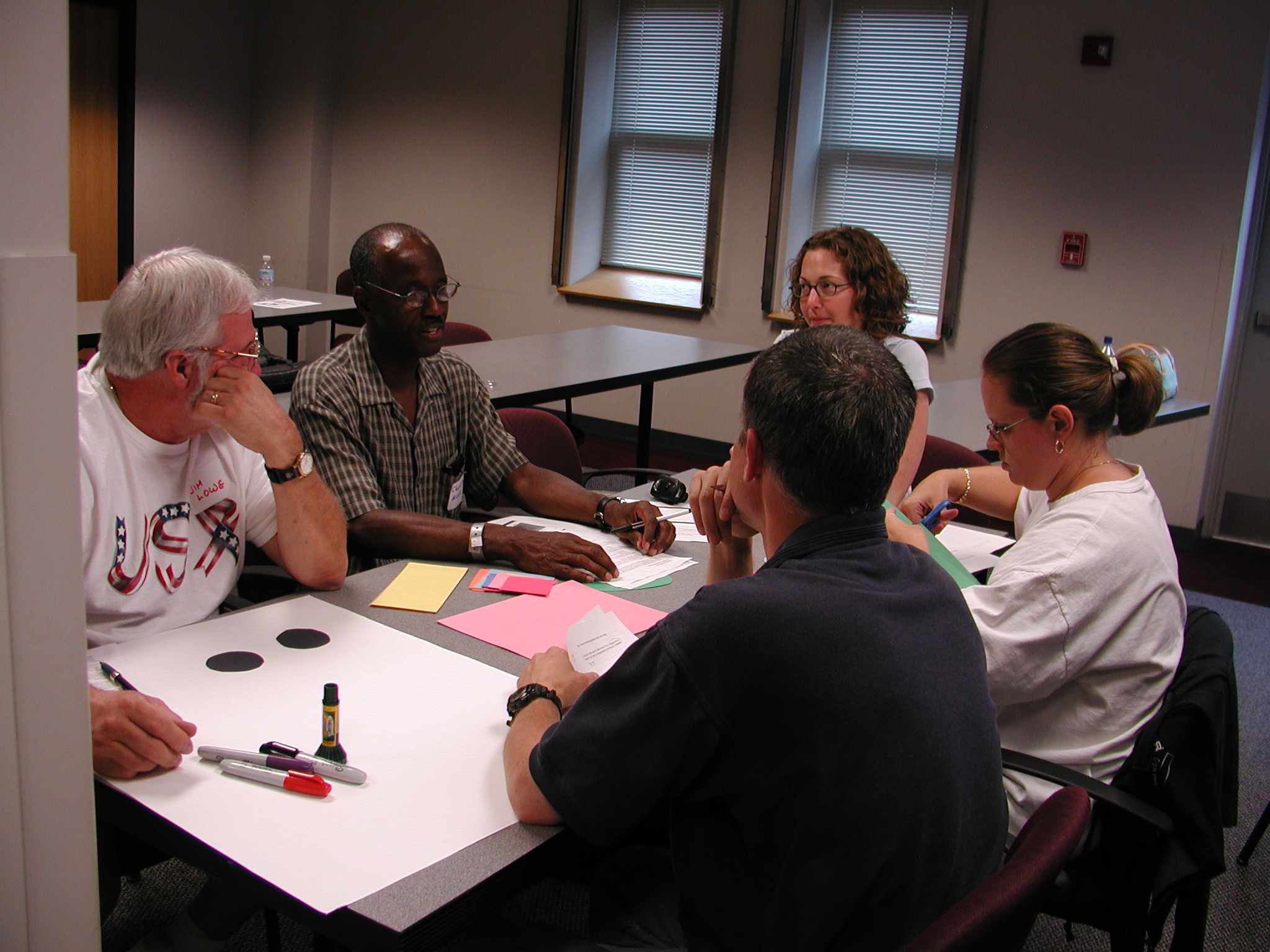 five adults working and talking around a table with pens and paper