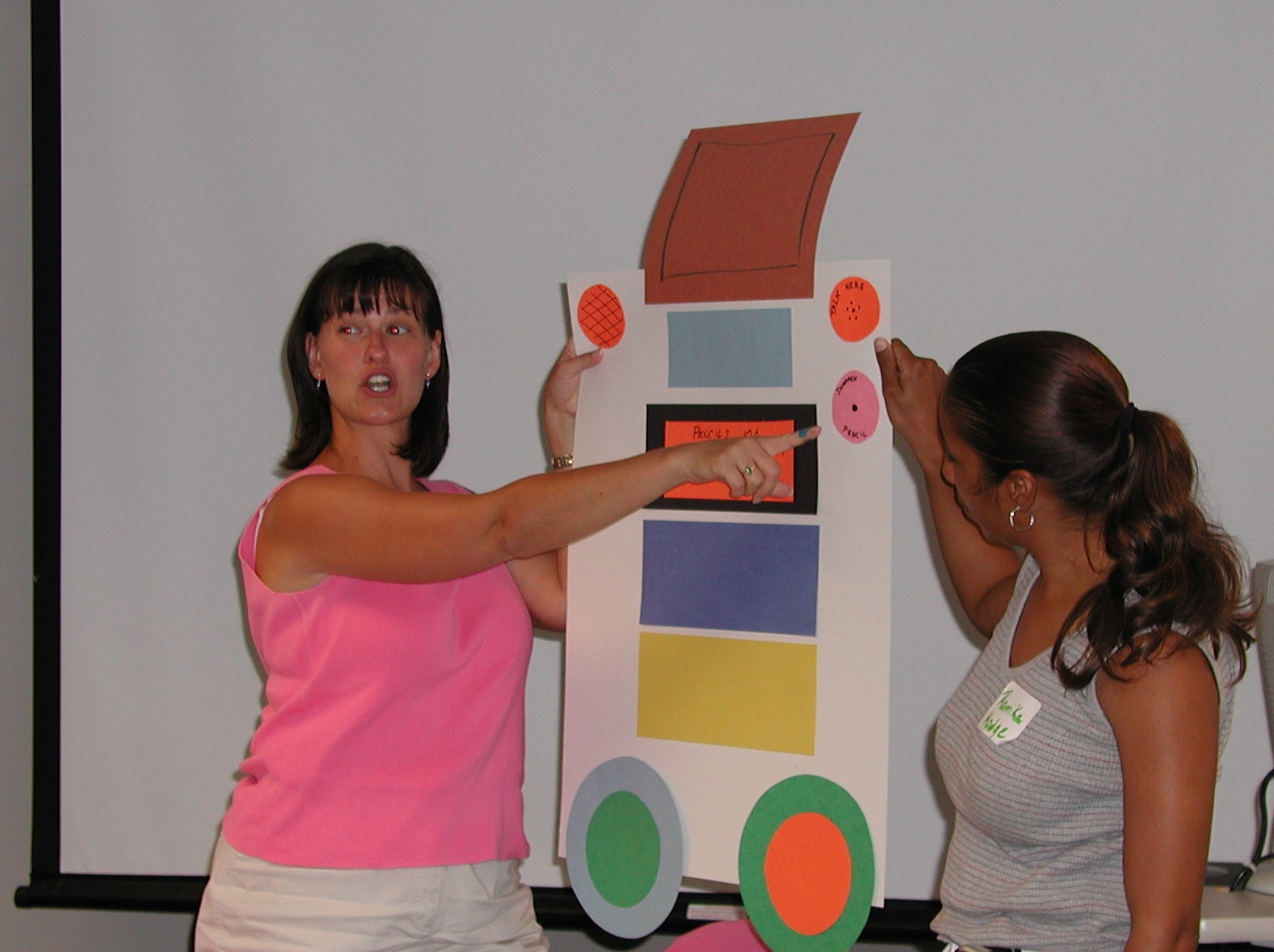 two women at the front of a classroom pointing to a design mock-up