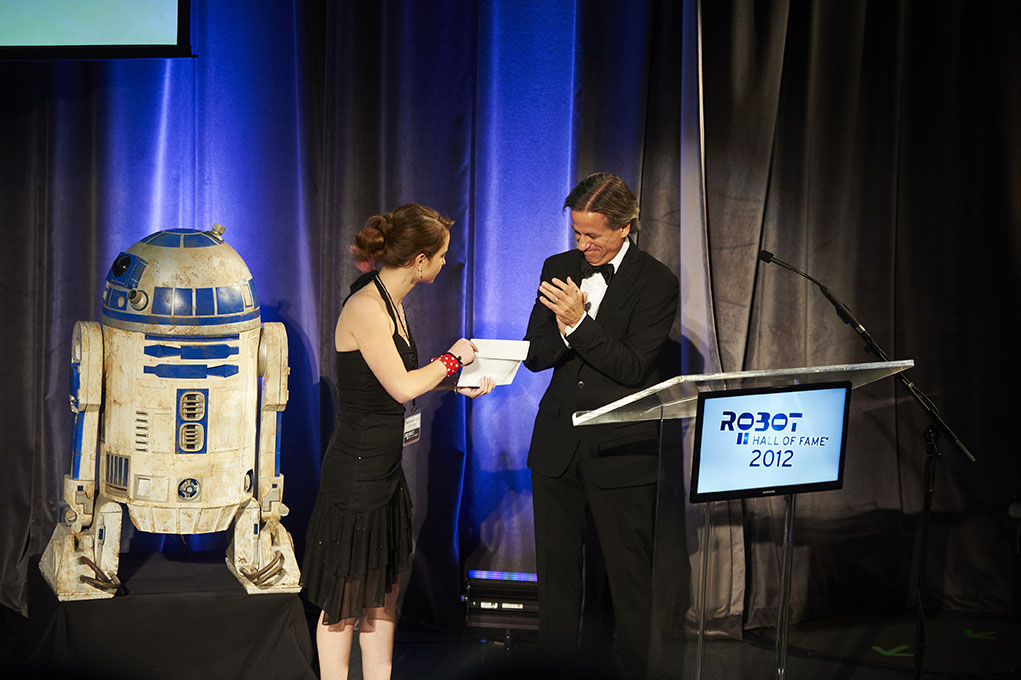A member of the Girls of Steel delivers the envelope containing the winner of the Robot Hall of Fame’s Research category to Henry Thorne, chief technology officer of 4Moms.