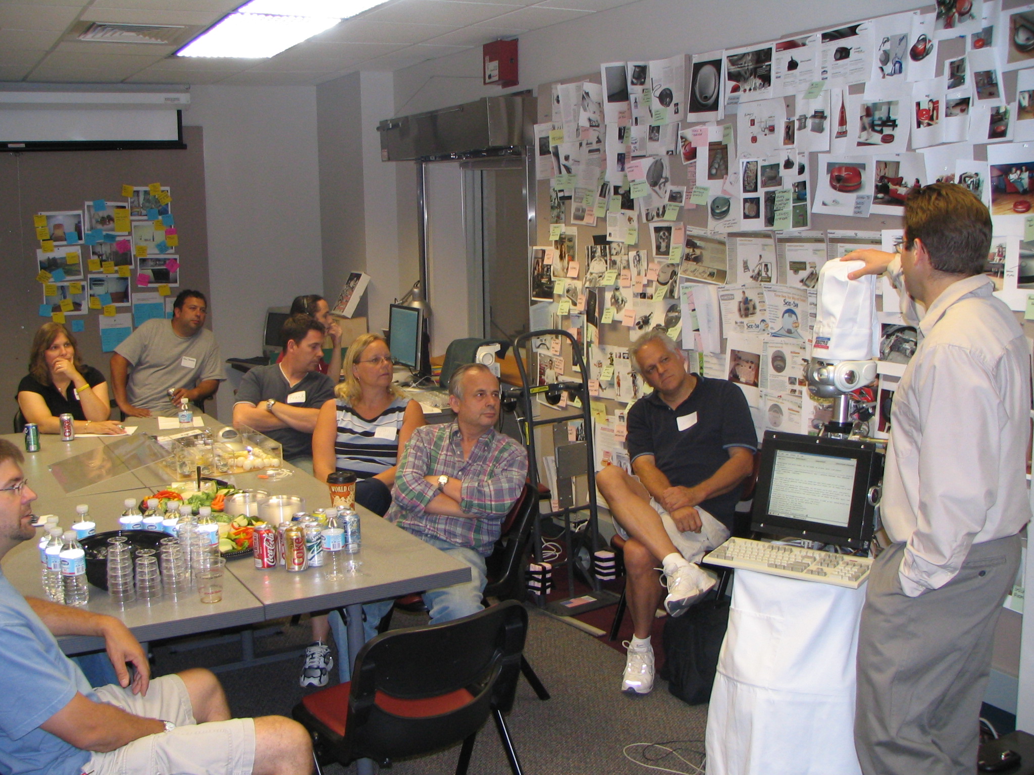 a large group of adults sitting around a table are watching a faculty member showing some equipment