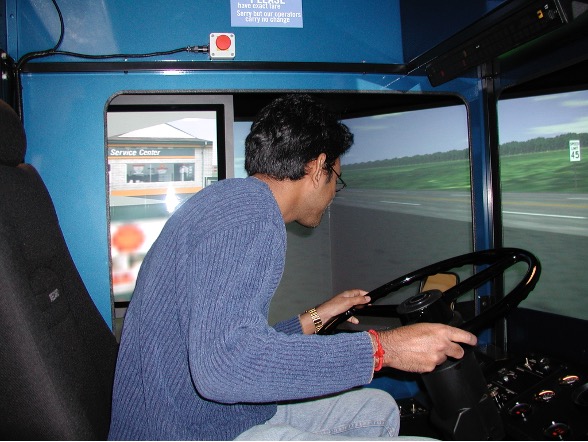 Student sitting inside a simulated city bus with his hands on the steering wheel
