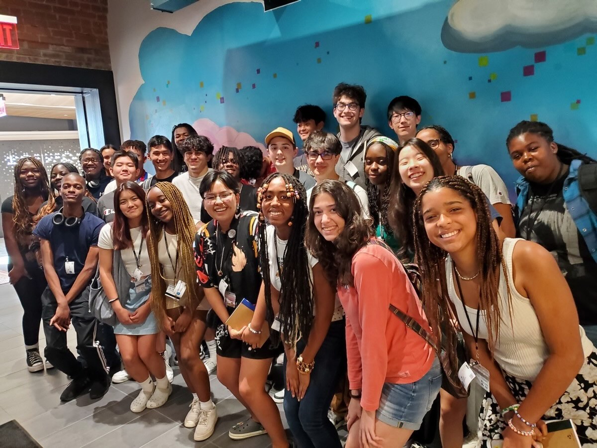 A group of students pose and smile for the camera against a bright blue wall.