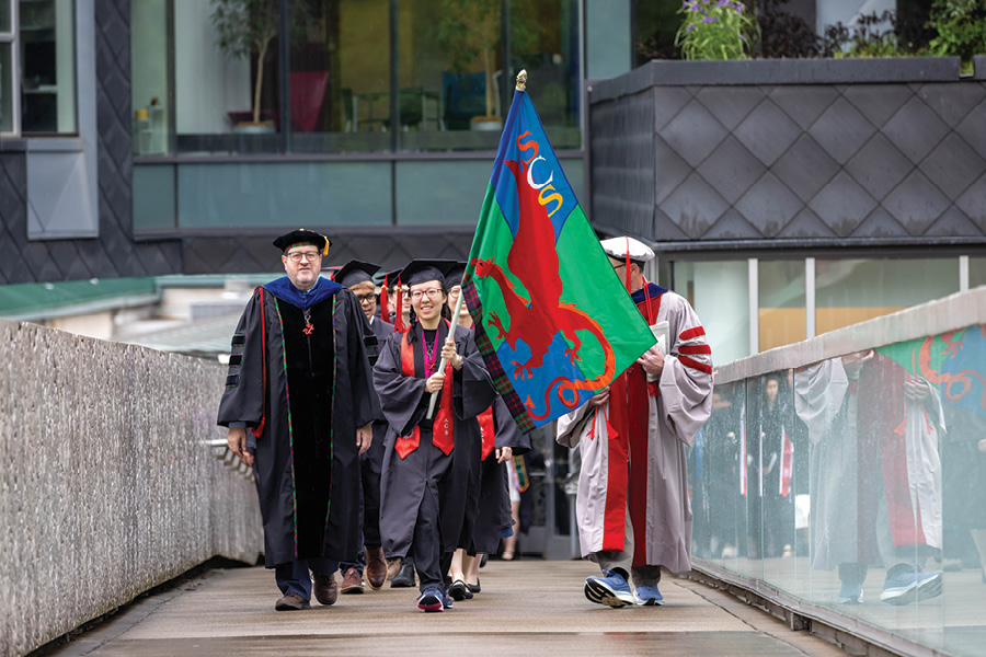  a picture of Tom Cortina and SCS students holding the SCS flag crossing the Pausch Bridge on CMU's campus