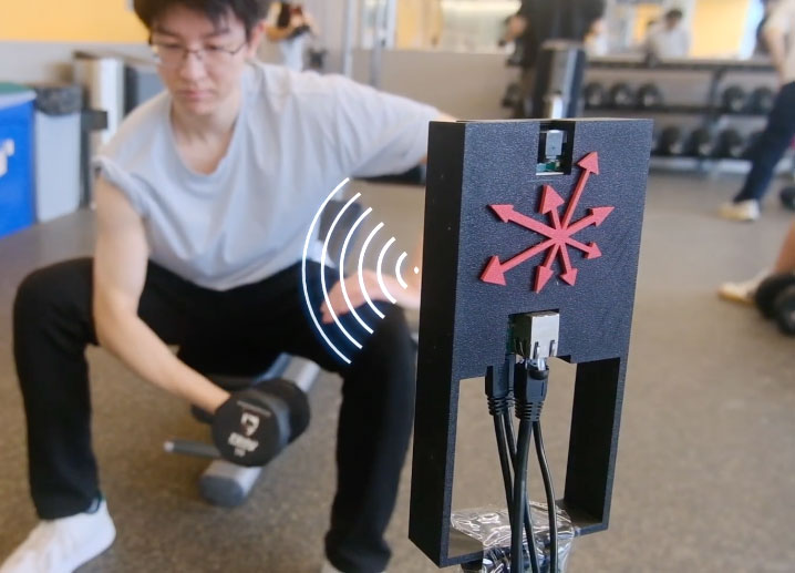  A man in the background sits on a bench and lifts a dumbell while a device in front of him monitors his muscle fatigue.