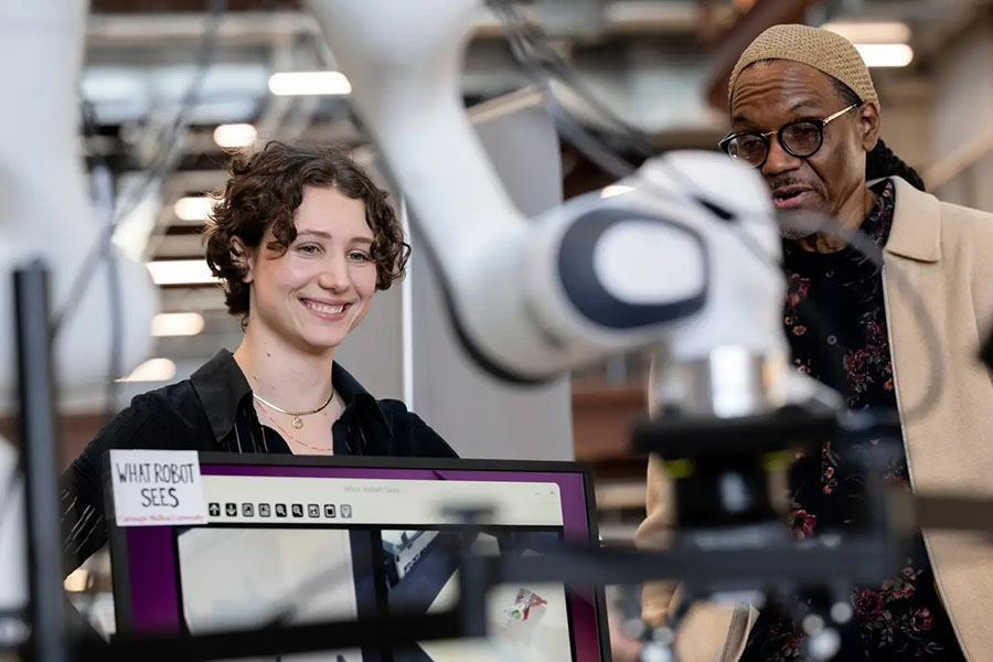  A man and woman look at a something, which upon reflecting is a robot arm that is slightly blurred but visible in the foreground.