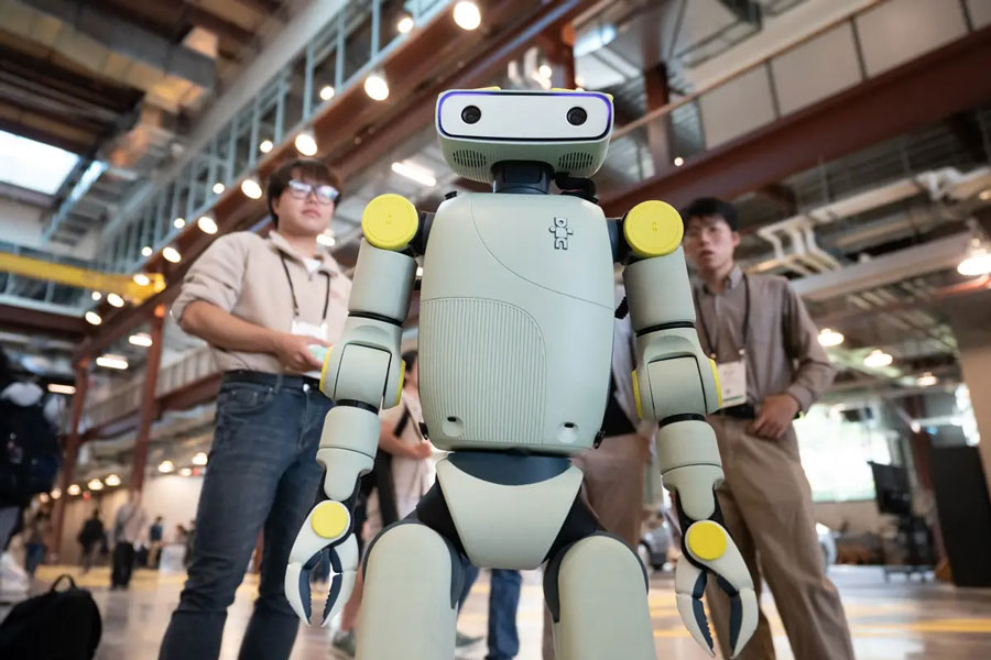  A humanoid robot, closeup, with human operators slightly blurred in the background.