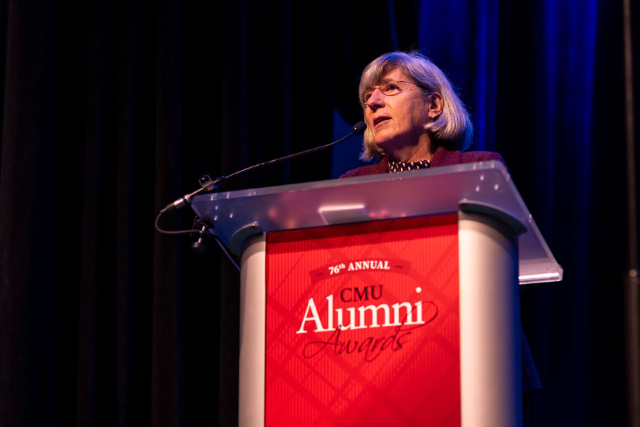  A woman stands at a podium in front of a dark background.