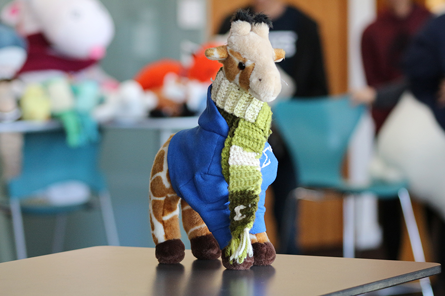 A stuffed giraffe wearing a blue hoodie and green scarf.