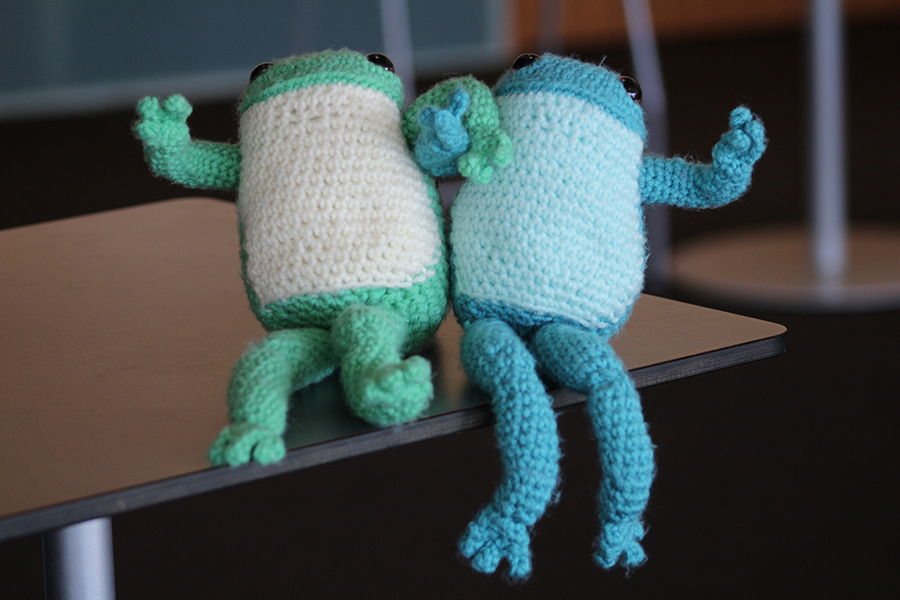 Two stuffed frogs, one green with a white stomach and one blue with a white stomach.