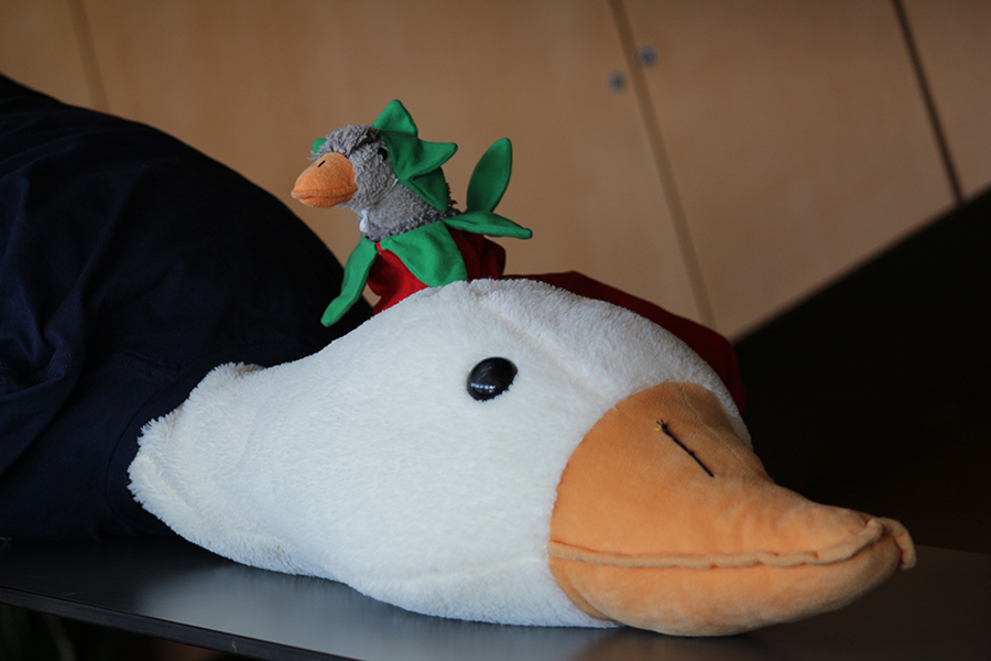 A small stuffed goose resting on the neck of a very large stuffed goose.