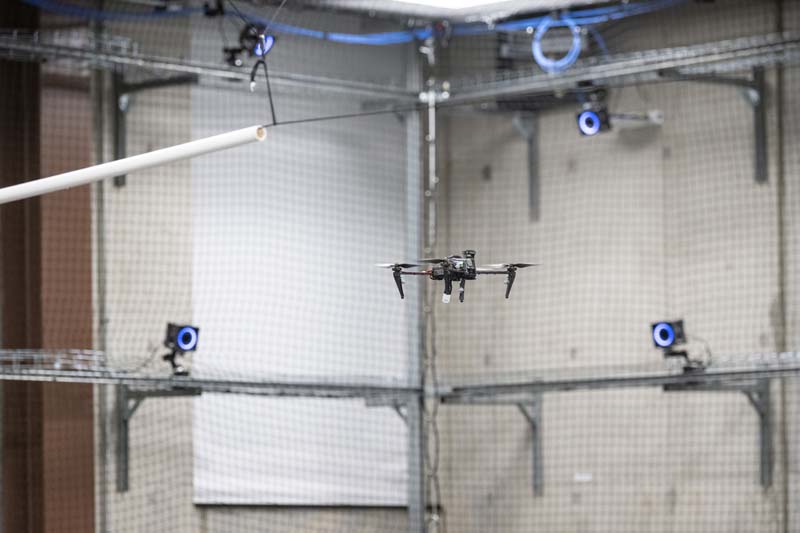 A drone flies inside an indoor drone cage.