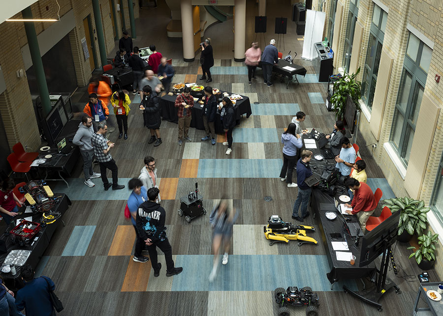 An overhead shot of a reception with humans and robots milling about in an atrium area of a building.