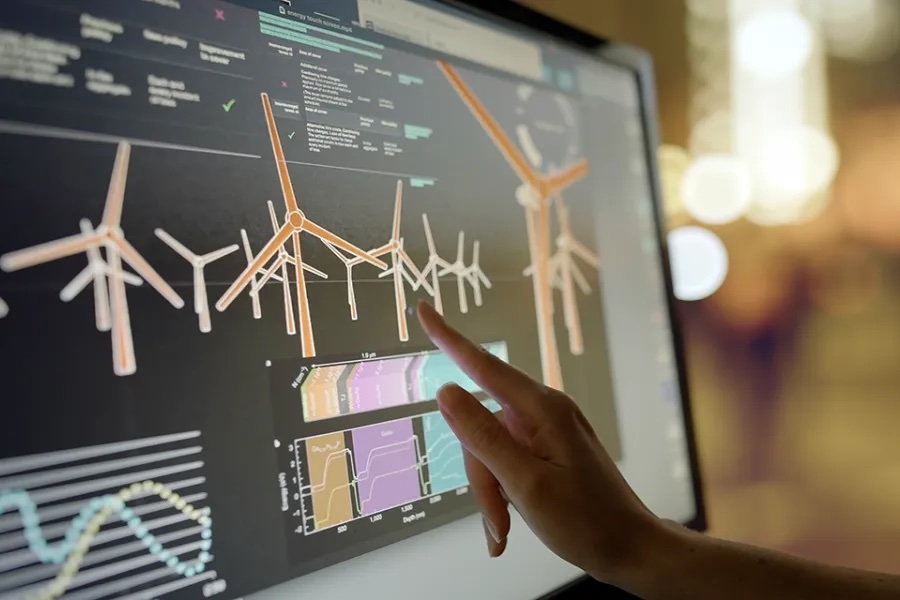 A human hand points at a wind turbine on a computer screen.