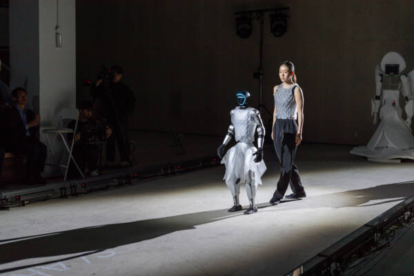  A robot and woman strut down a runway.