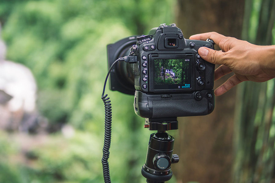 A digital camera on a tripod in the foreground against a blurry forested background.