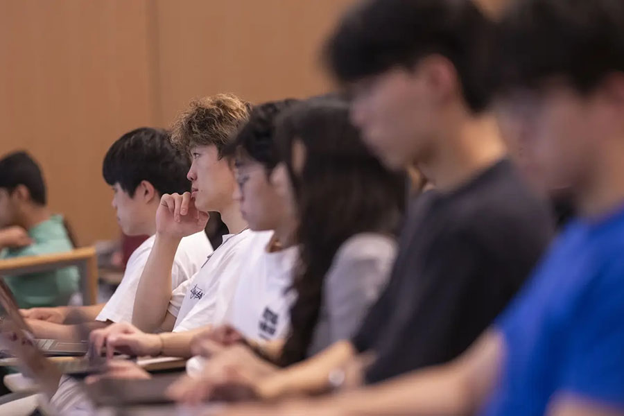  A row of students sitting in a classroom, some in focus and some blurred.