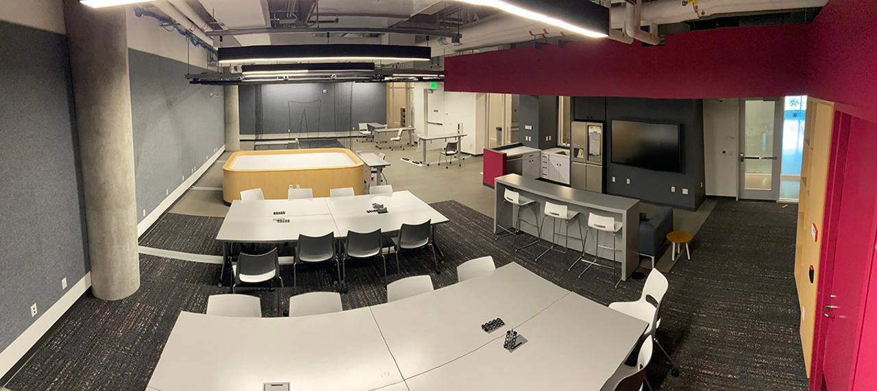 This photo shows the AI Maker Space from above, including open areas for collaboration, a net-covered area for drone research and a smart home section with kitchen appliances.
